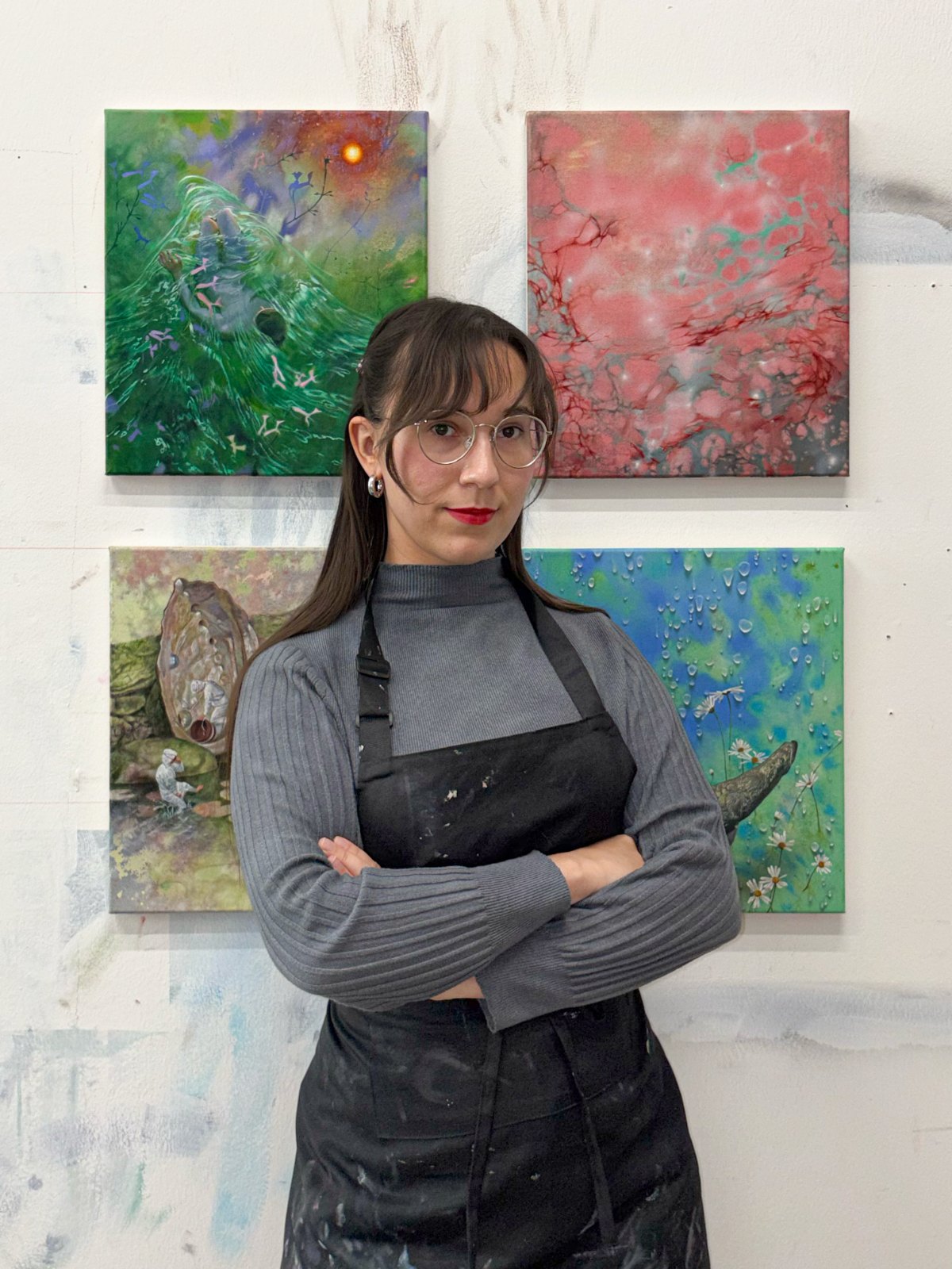 Margarita Montgomery standing with arms crossed in front of four of her paintings in the studio